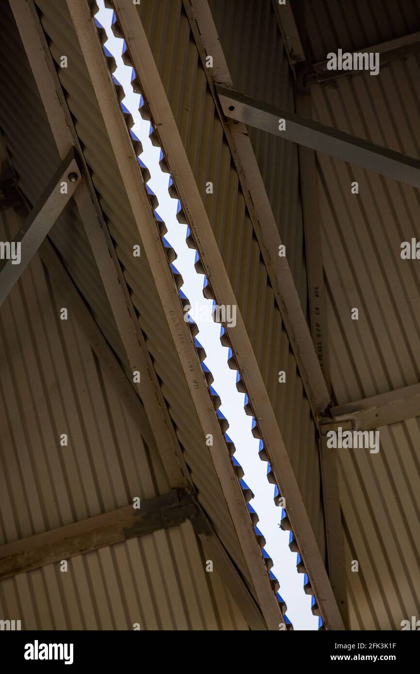 Geripptes Metallprofildach eines Industriegebäudes oder Hangars. Abstrakte Ansicht. Blauer Himmelsstreifen auf dem Hintergrund. Stockfoto