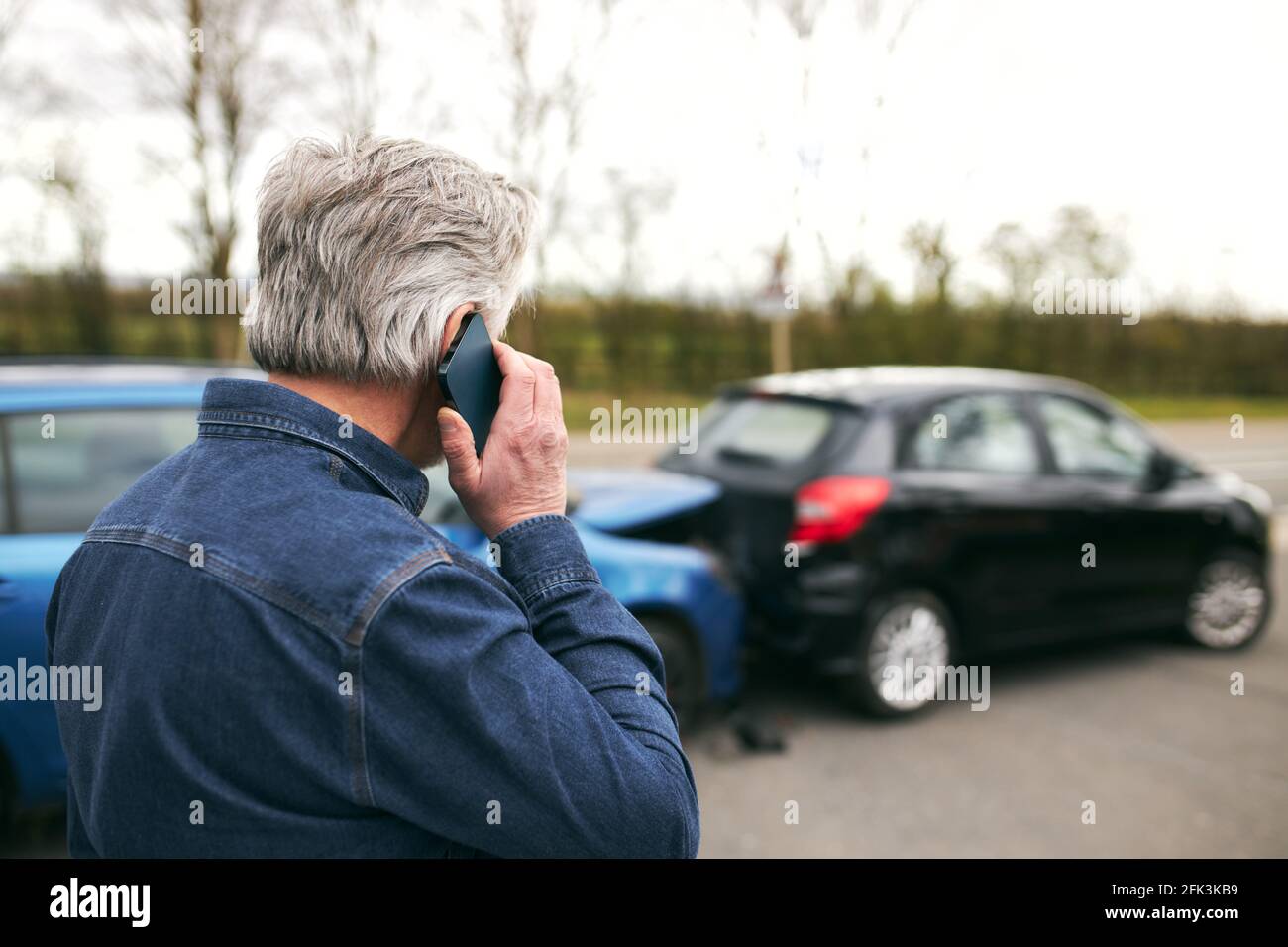 Rückansicht des älteren männlichen Fahrers, der neben einem beschädigten Fahrzeug steht Nach Verkehrsunfällen, die den Vorfall über ein Mobiltelefon an die Versicherungsgesellschaft melden Telefon Stockfoto