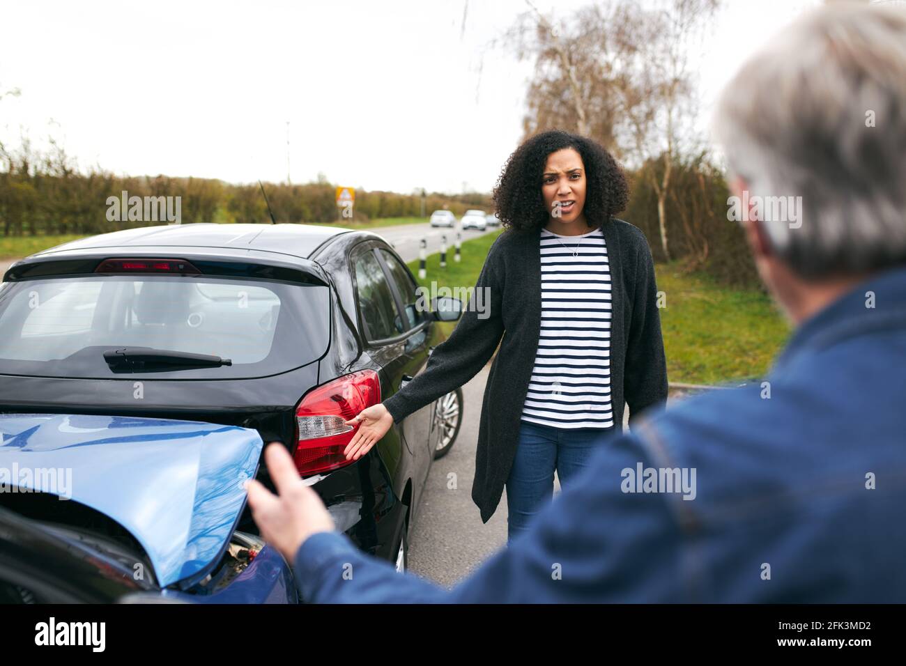 Älterer männlicher Fahrer, der mit über die Schuld für den Autounfall argumentiert Eine jüngere Autofahrerin Stockfoto