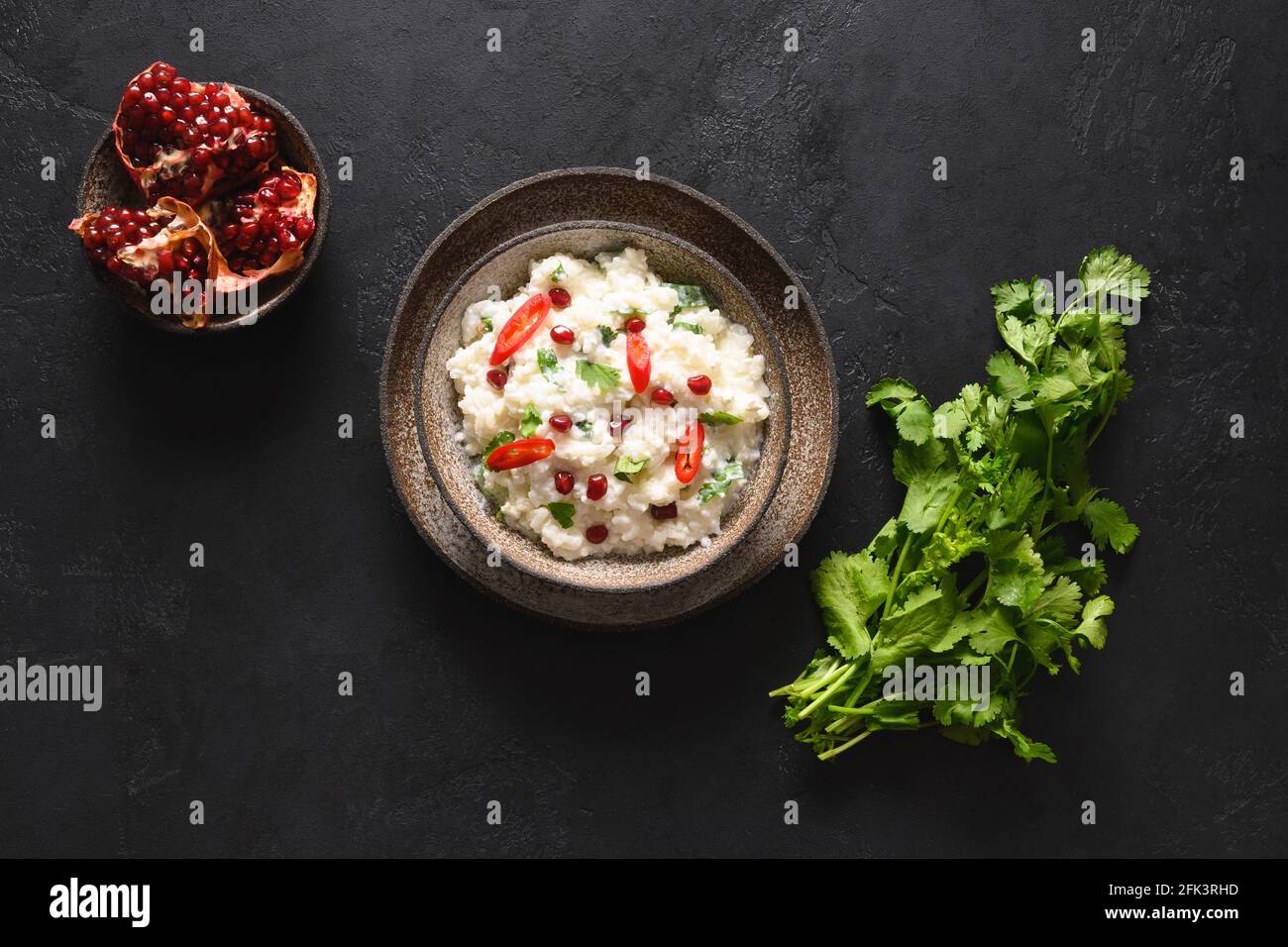 Quark mit Granatapfel, Koriander, Senfkörnern, Ingwer auf schwarzem Hintergrund. Indische Südküche Stockfoto
