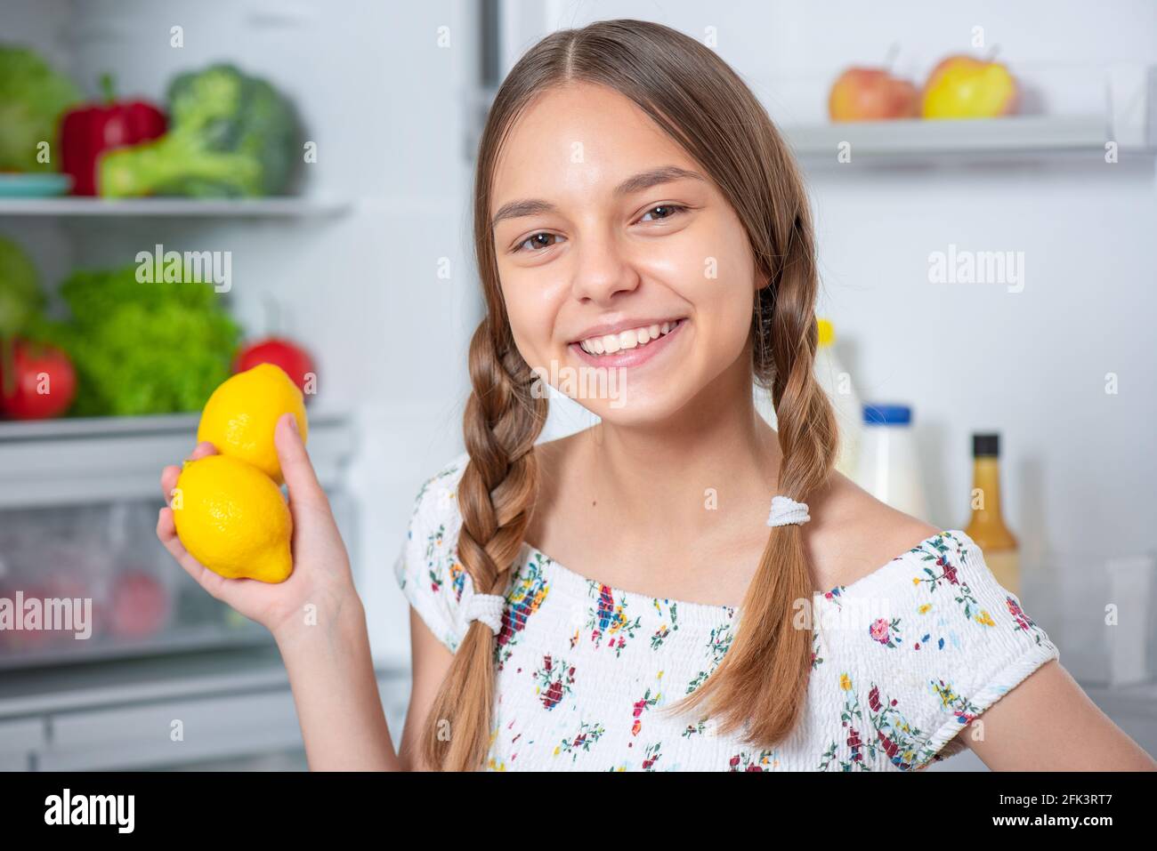 Schöne junge glücklich teen Mädchen hält frische gelbe Zitronen während Stehen in der Nähe von offenem Kühlschrank in der Küche zu Hause Stockfoto