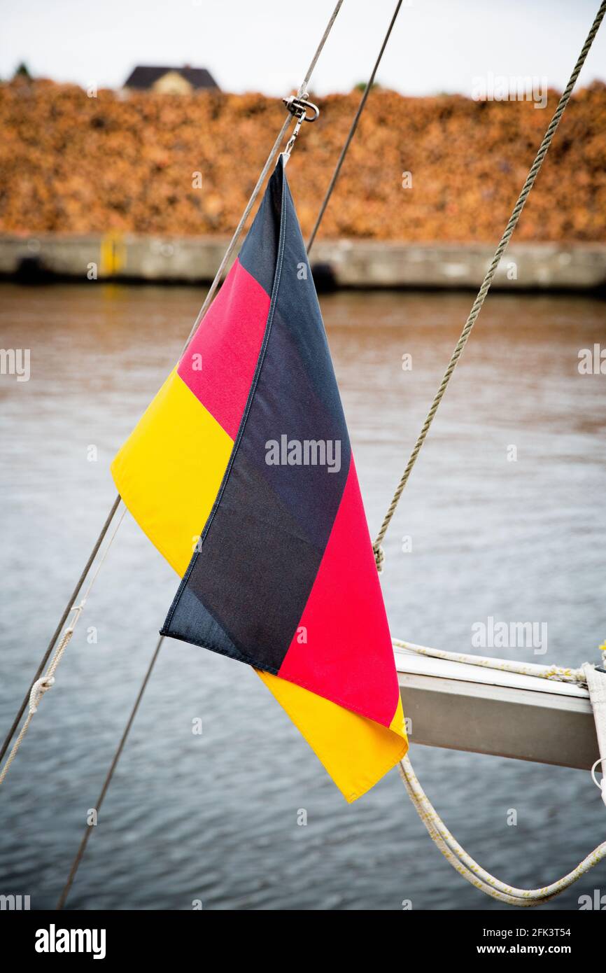 Deutschland Flagge auf EINEM Boot im Hafen, im Hintergrund Holzstapel, Holzlager, versandbereit. Stockfoto