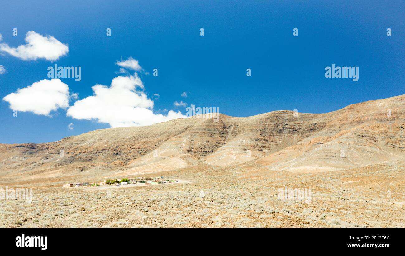 Abgelegenes Dorf in einer Wüstenlandschaft am Fuße des Eine Hügelkette aus der Ferne Stockfoto