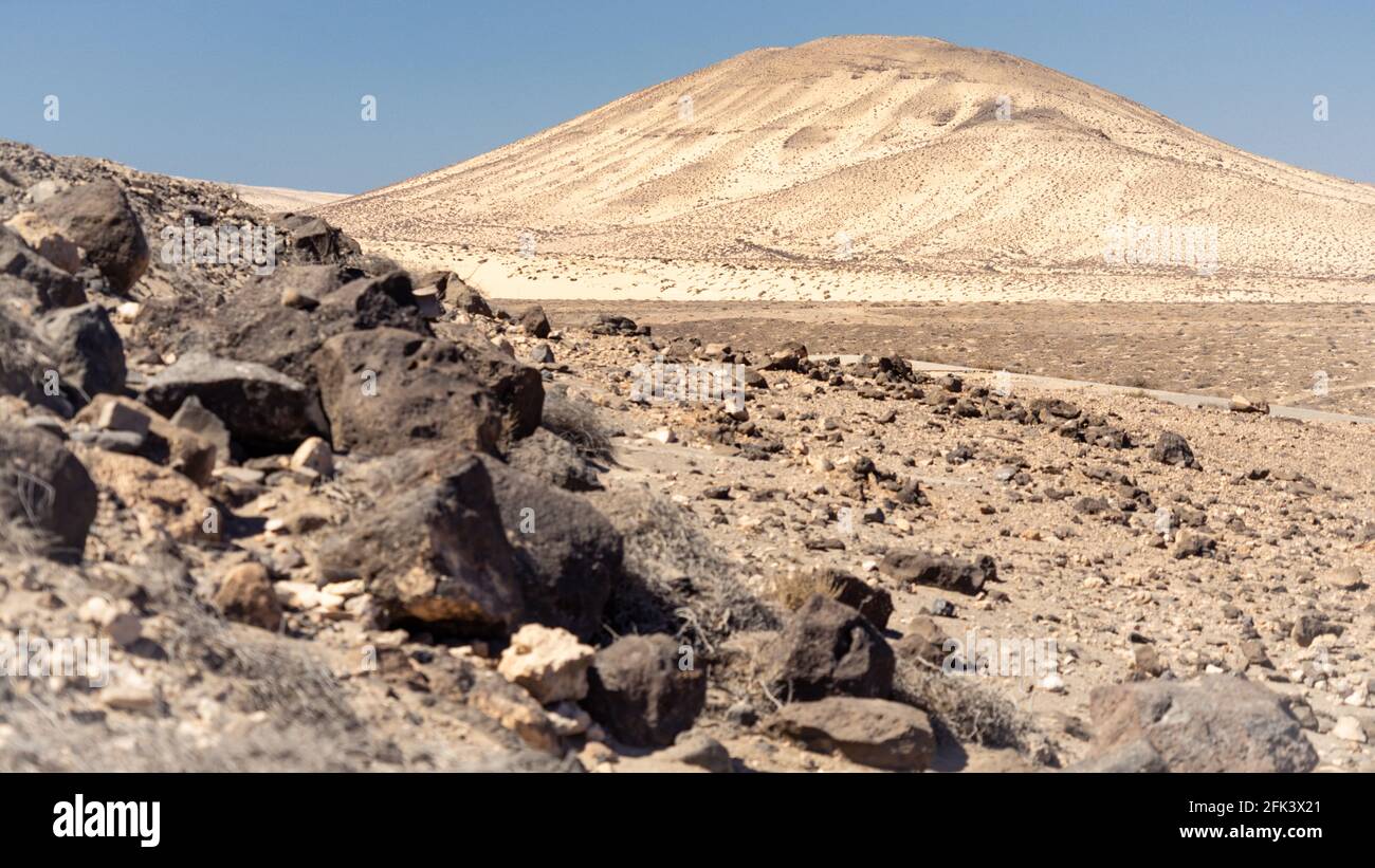 Weiße Hügel mit schwarzen Lavagesteinen in einer Wüste Landschaft unter einem blauen wolkenlosen Himmel Stockfoto
