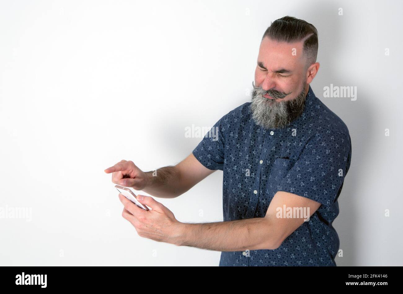 Hipster mit großem grauen Halbbart, mit seinem Smartphone mit einem angewiderten Gesicht. Kaukasisch 40-45 Jahre Stockfoto