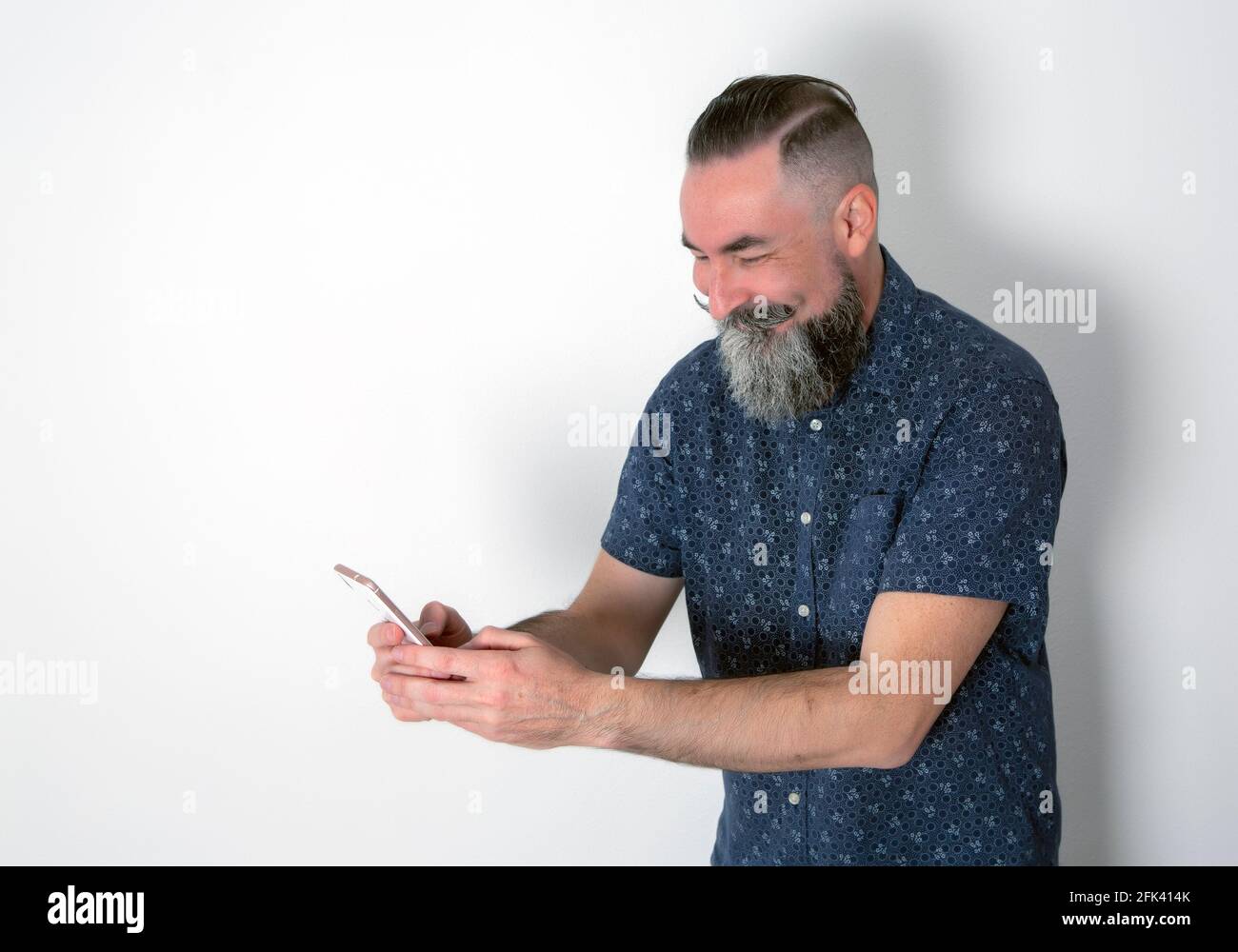Der kaukasische 40-45-jährige bärtige Hipster schaut sich sein Handy an Telefonieren Sie mit einem fröhlichen und lachenden Gesicht Stockfoto