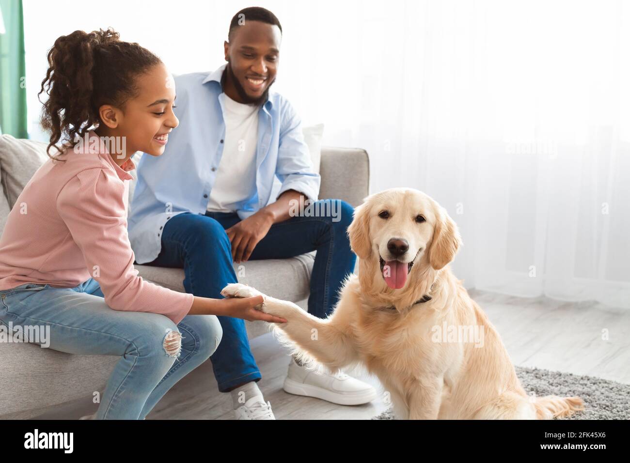 Lächelndes schwarzes Mädchen, das im Wohnzimmer mit einem Haustier spielt Stockfoto