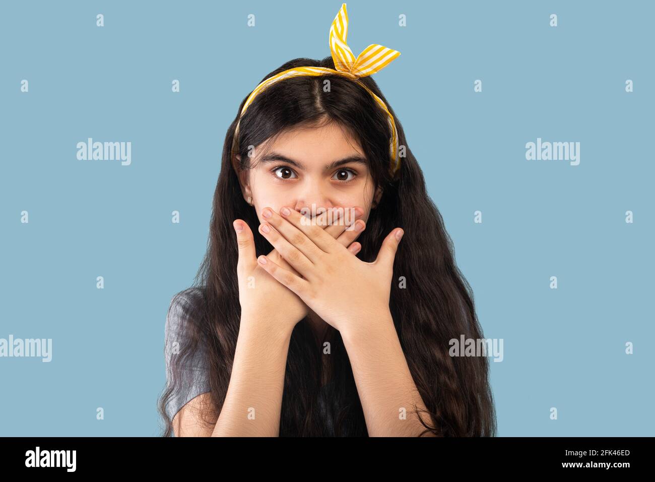 Schockiert indischen Teenager-Mädchen bedeckt ihren Mund mit Händen und Blick auf die Kamera, halten Schweigen auf blauem Hintergrund Stockfoto