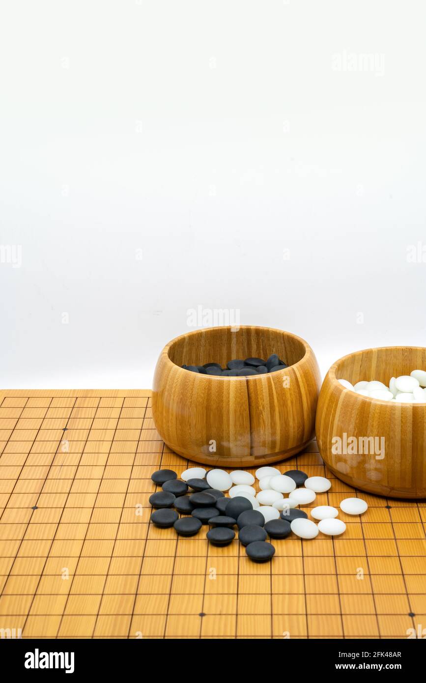 Isoliertes traditionelles Brettspiel von China und Japan, genannt Go, zwei offene Holzschalen aus schwarzen Steinen und weißen Steinen. Das vertikale Bild auf weiß b Stockfoto
