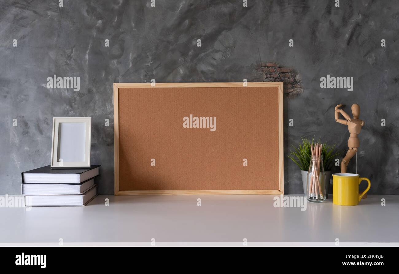 Weißer Arbeitsbereich mit Korkbrett und Becher, Büromaterial und Buch am Arbeitsplatz im Heimbüro Stockfoto