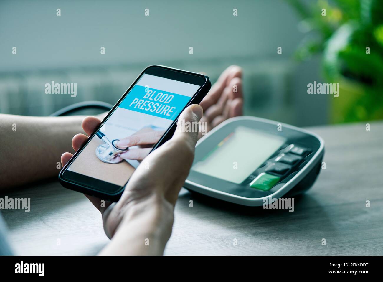 Ein kaukasischer Mann, der an einem Tisch sitzt, misst seinen Blutdruck mit  einem elektronischen Blutdruckmessgerät, während er sein Smartphone in den  Händen hält Stockfotografie - Alamy