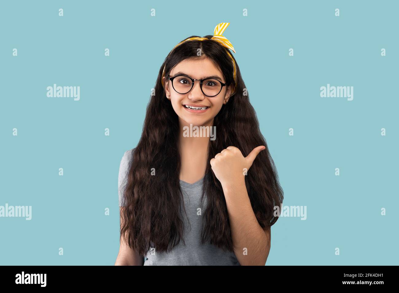 Glücklicher indischer Teenager zeigt zur Seite, mit dem Daumen nach oben auf blau studio-Hintergrund Stockfoto