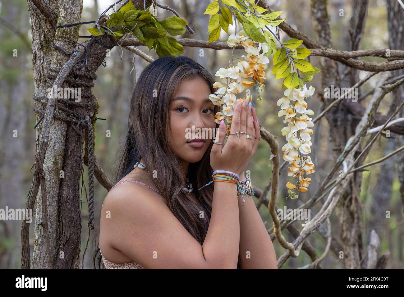 Nahaufnahme einer jungen Frau mit langen braunen Haaren in einer bewaldeten Umgebung, mit Blumen, die an einer Weinrebe hängen Stockfoto