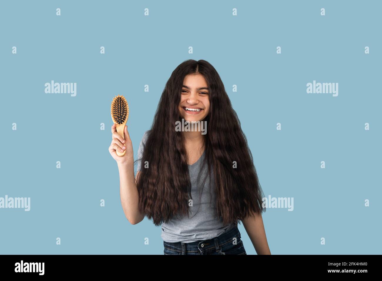 Portrsit von schönen indischen Teenager-Mädchen mit langen dunklen Haaren Halten Sie einen Holzpinsel und lächeln Sie auf blauem Hintergrund auf die Kamera Stockfoto