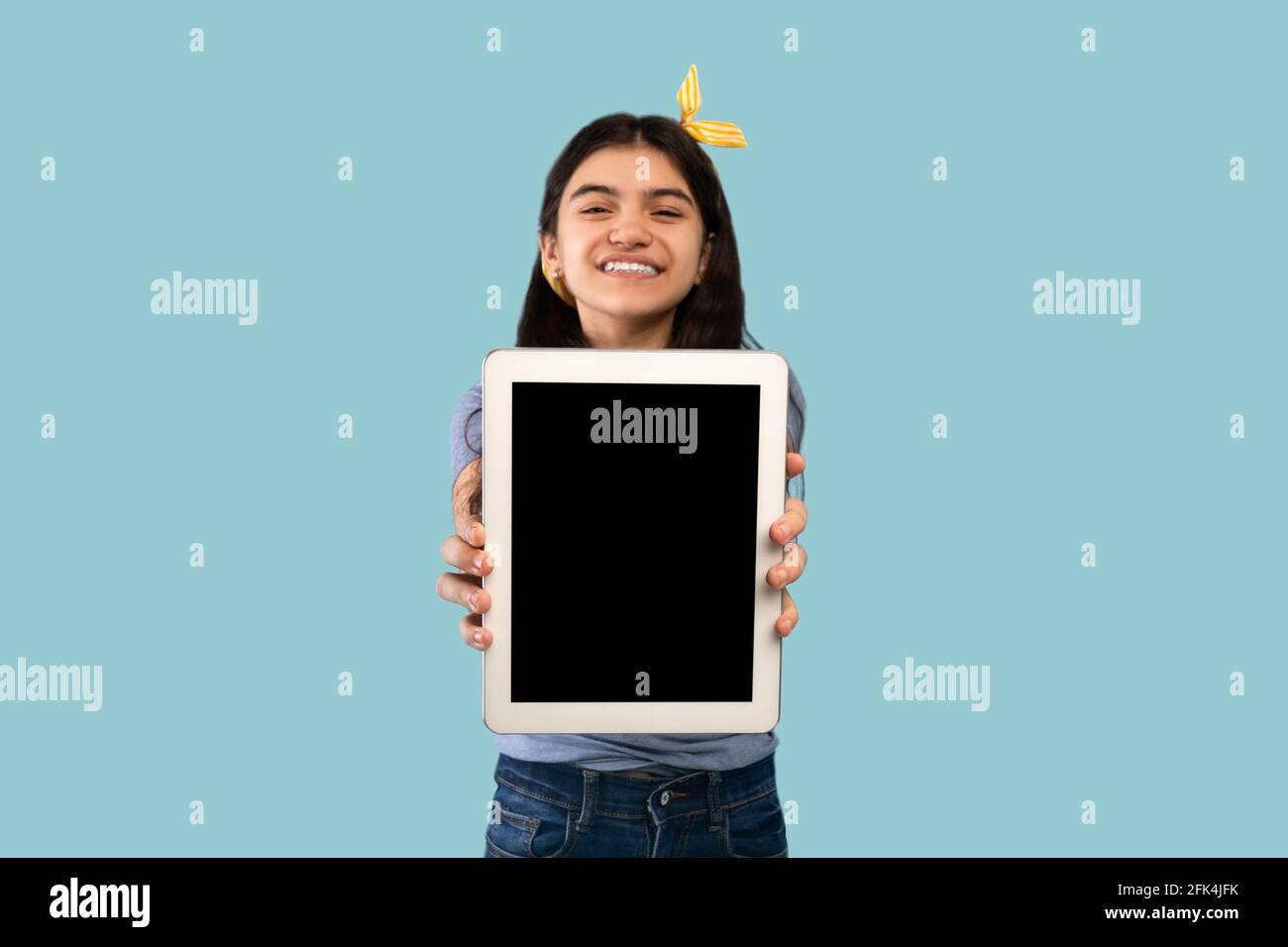 Fröhlicher indischer Teenager, der Tablet-Computer mit Mockup für die Website zeigt Oder App-Design auf blauem Studiohintergrund Stockfoto