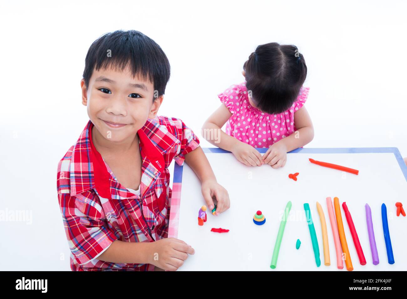 Kleine asiatische Kinder spielen und erstellen Spielzeug aus Spielteig auf dem Tisch. Junge lächelnd und Blick auf die Kamera, auf weißem Hintergrund. Stärken Sie das imagi Stockfoto