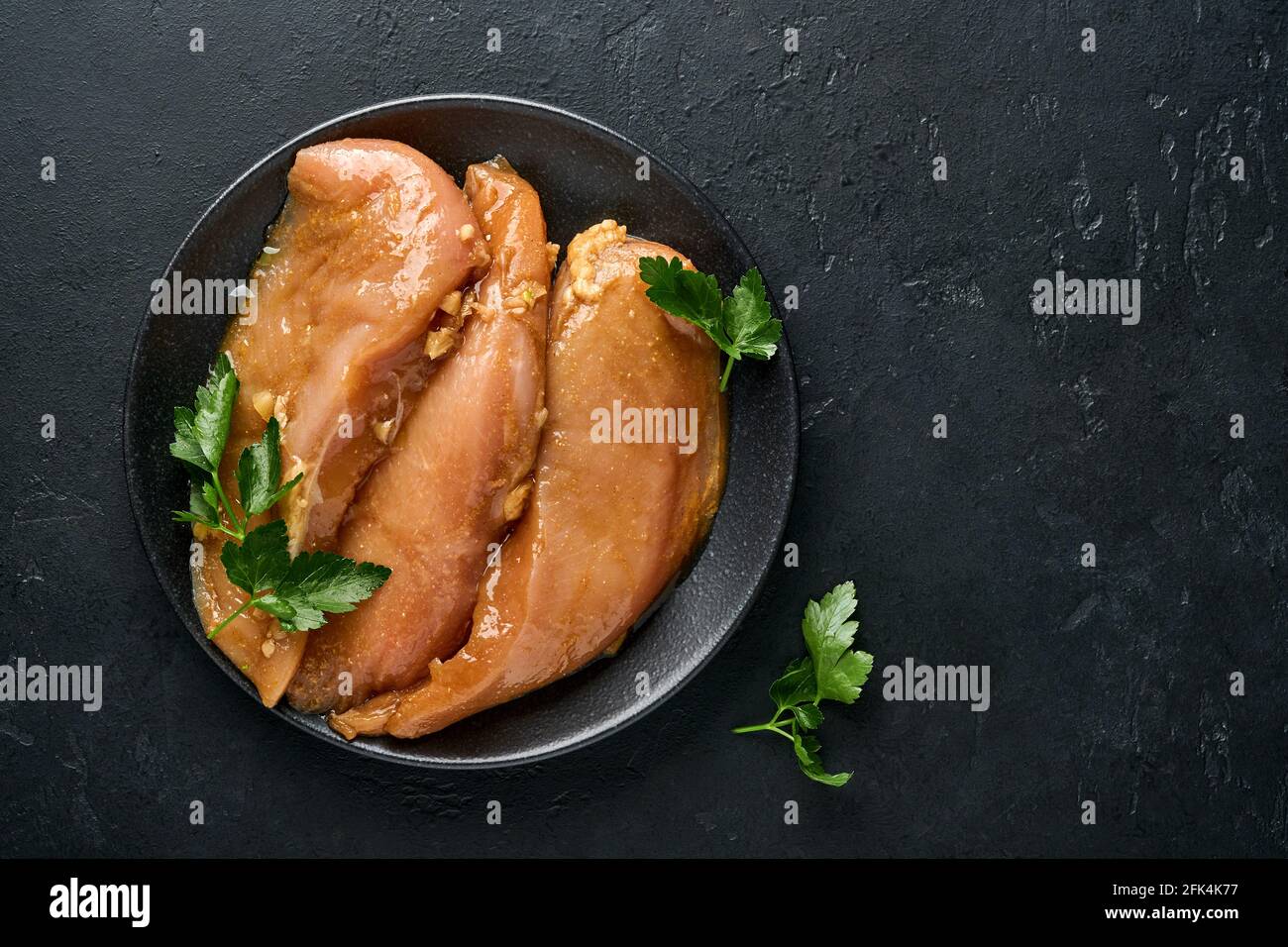 Rohes Hühnerfleischfilet, mariniert in Teriyaki-Sojasauce, Zwiebeln, Knoblauch und Pfeffer auf schwarzem Teller auf dunklem Schiefer, Stein oder Beton. Obere V Stockfoto