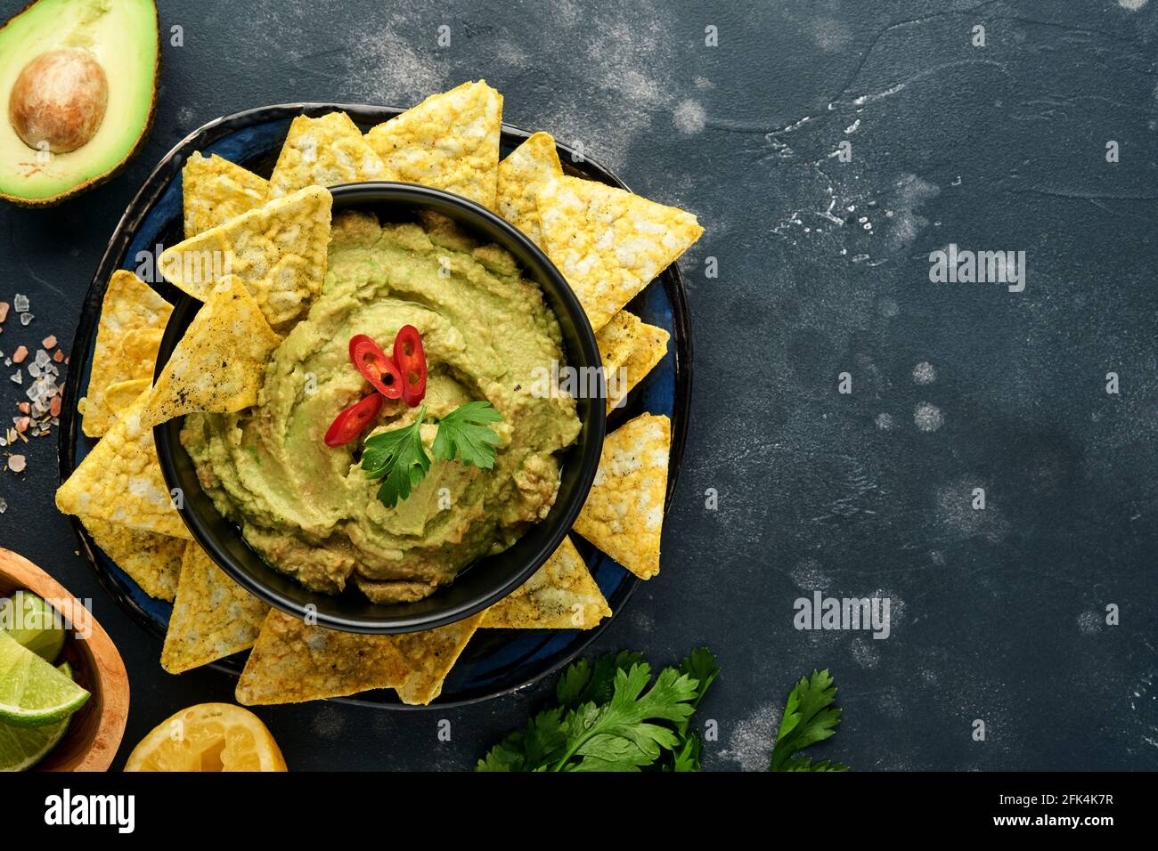 Guacamole. Traditionelle lateinamerikanische mexikanische Dip-Sauce in einer schwarzen Schüssel mit Avocado und Zutaten und Maisnachos. Avocadoverbreitung. Draufsicht. Copyspa Stockfoto