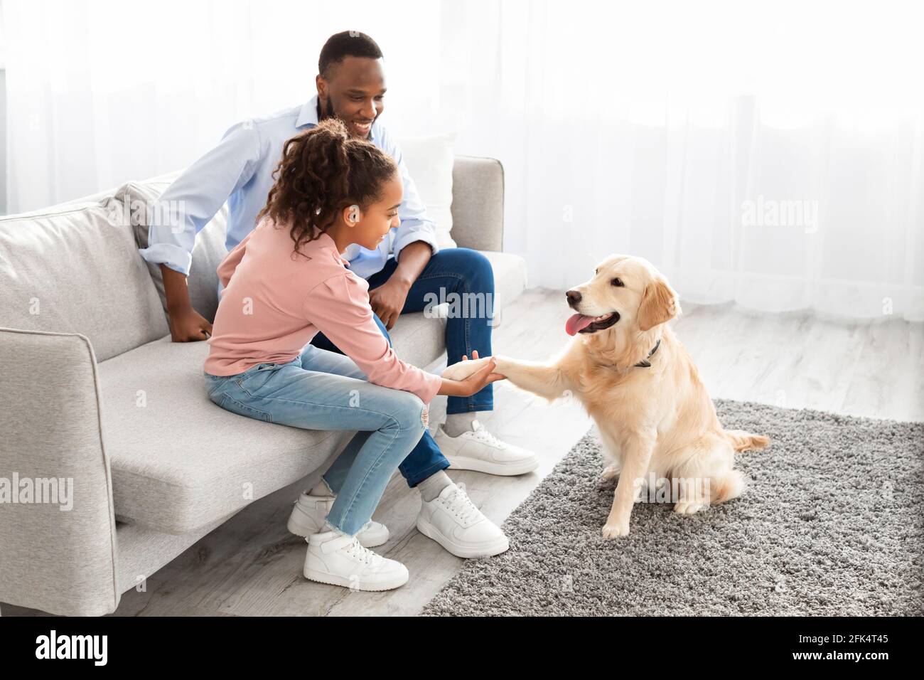 Lächelndes schwarzes Mädchen, das im Wohnzimmer mit Hund spielt Stockfoto