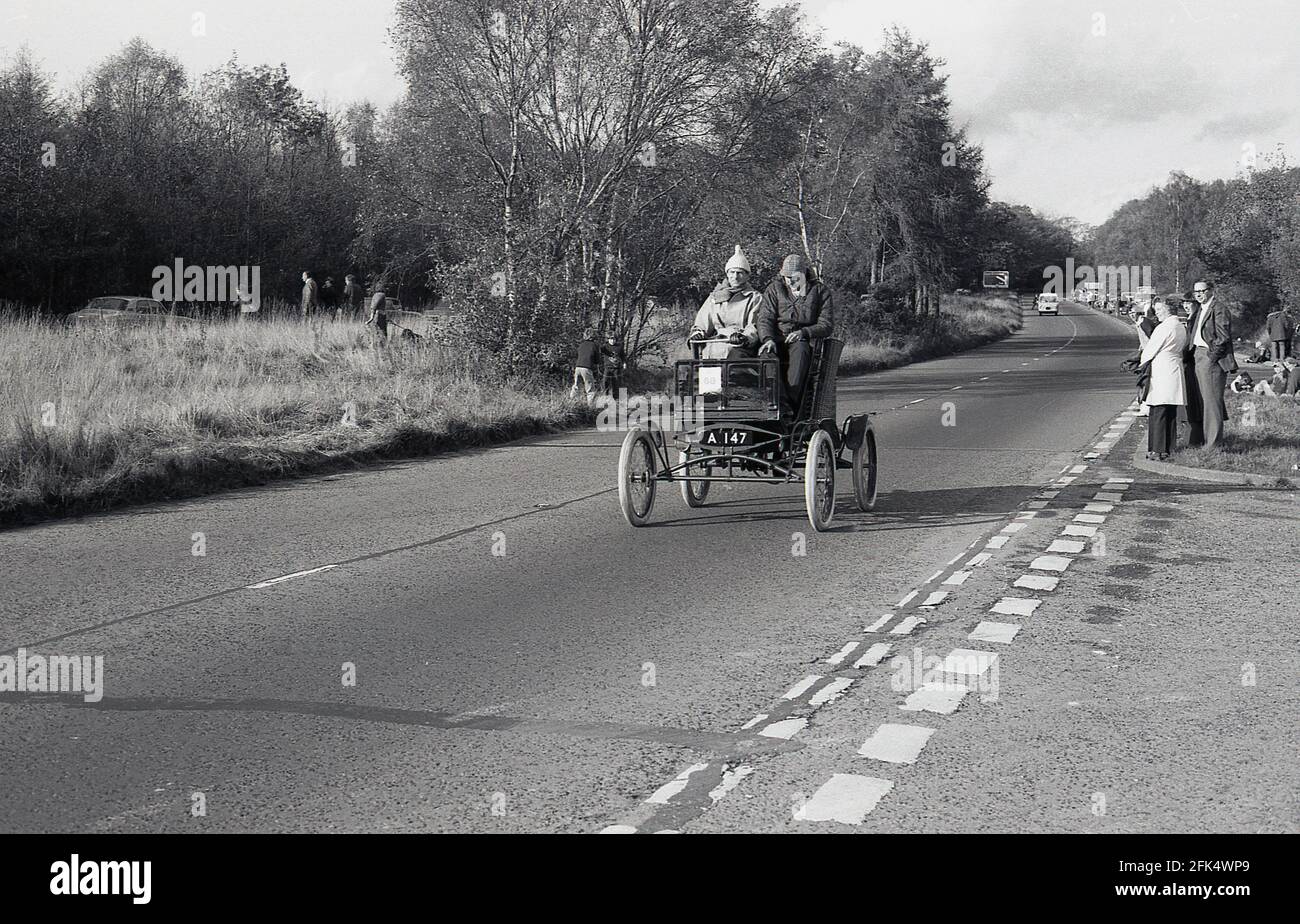In den 1980er Jahren, auf einer Straße mit zwei Wagen, fahren zwei Männer in einem alteingesessenen Auto, das an der historischen jährlichen Autofahrt, dem Veteran Car Run von London nach Brighton, teilnimmt, der vom RAC organisiert wird. Die längste Motorveranstaltung der Welt steht nur Automobilen offen, die vor 1905 gebaut wurden. Der erste Automobilclub im Vereinigten Königreich wurde 1896 gegründet, der die Light Locomotives on the Highway Act feierte, der die Geschwindigkeitsbegrenzung auf 14 km/h erhöhte und die Notwendigkeit für Autos abschaffte, denen ein Mann zu Fuß mit einer roten Flagge vorausging. Stockfoto