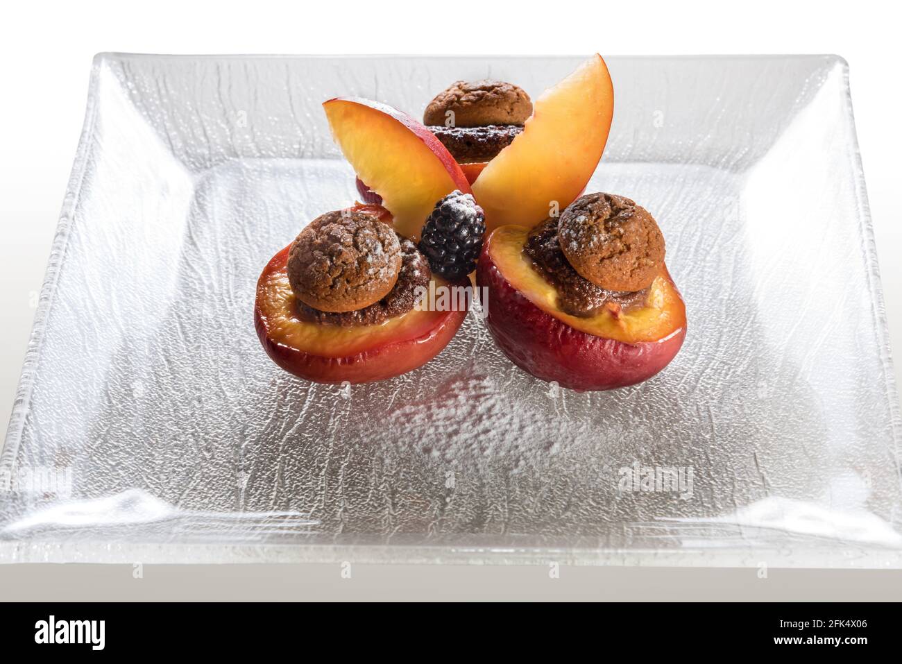 Gebackene Obstpfirsiche gefüllt mit Schokolade und Amaretti-Keksen, typisch piemontesisches Dessert, Italien, auf Glasplatte Stockfoto