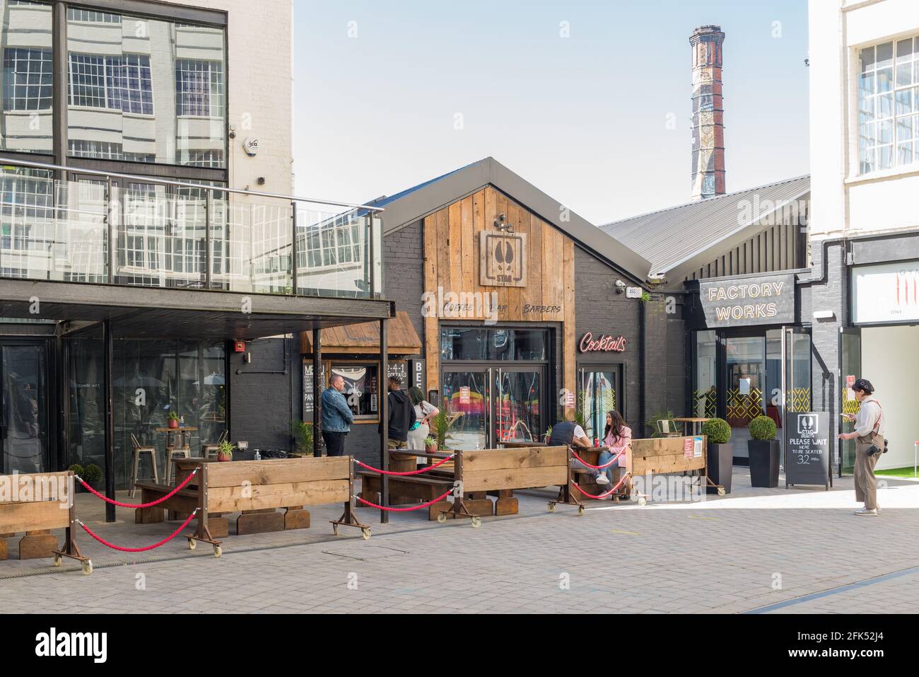 Menschen, die draußen sitzen und im Innenhof im Kreativviertel der Custard Factory in Digbeth, Birmingham, Großbritannien, essen und trinken Stockfoto