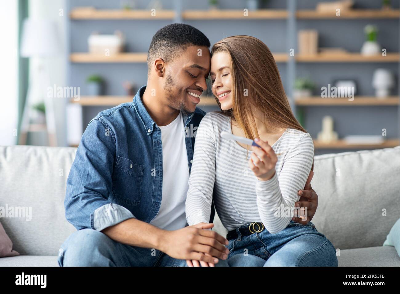 Eltern Werden. Romantische Multirassische Ehegatten Mit Positivem Schwangerschaftstest Zu Hause Stockfoto