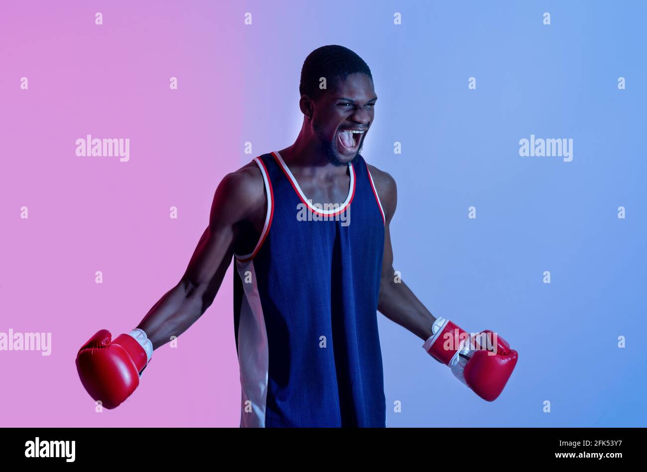 Aggressiver schwarzer Sportler in Boxhandschuhen, der im Neonlicht wütend schreit. Kampfsportkonzept Stockfoto