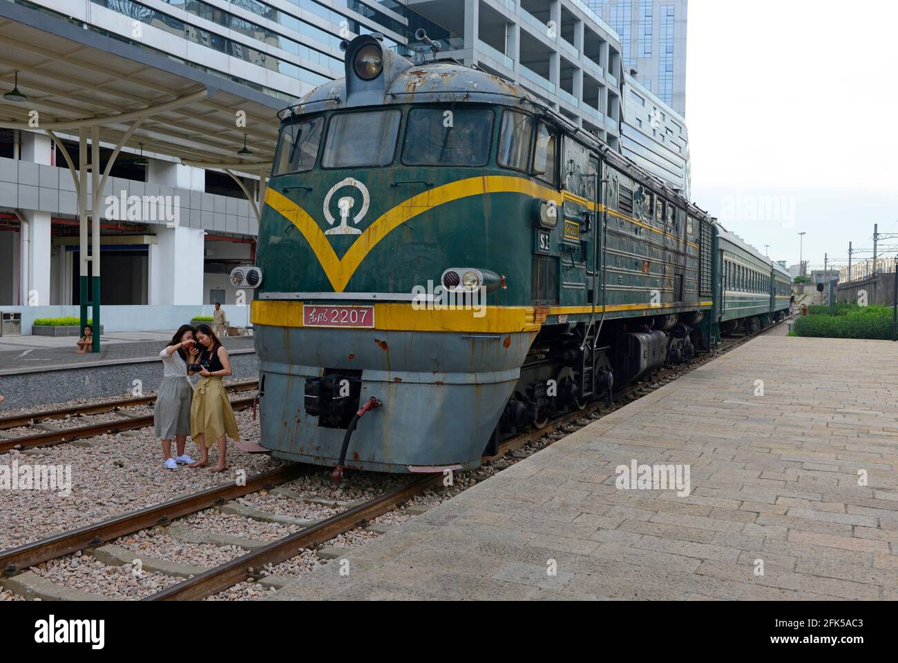 Zwei Frauen schauen sich die Fotos an, die sie in einem Park mit alten Bahngleisen, einem Bahnsteig und einem alten Zug mit Cowcatcher in Shenzhen, China, gemacht haben Stockfoto
