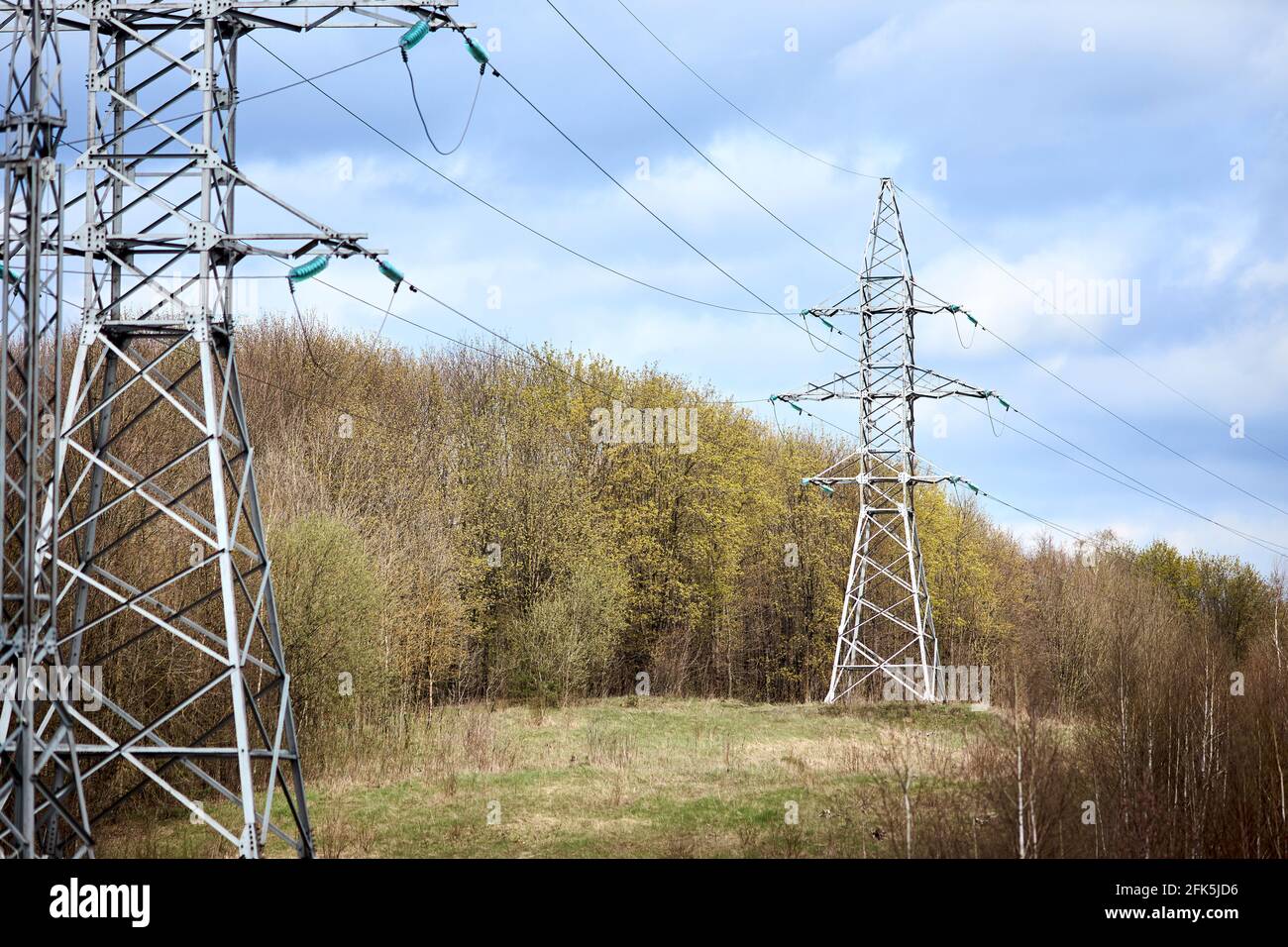 Hochspannungs-elektrischer Hochspannungs-elektrischer Sendeturm mit elektrischer Glasinisolator von über bewölktem stürmischen dunklen Himmel in der Nähe des Frühlingswaldes. Stockfoto