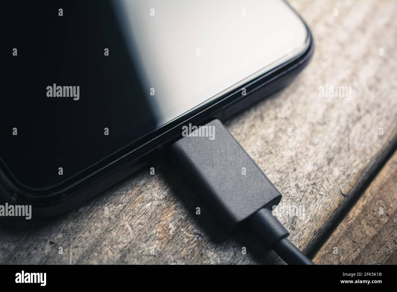 Schwarzes Smartphone mit angeschlossenem schwarzen USB-Kabel auf EINEM Holz Platine Stockfoto