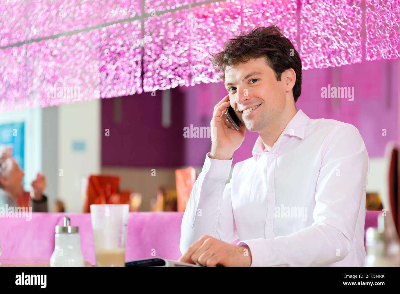 Junger Mann in einem Café oder Eis-Salon mit seinem Telefon, vielleicht ist er single oder jemand wartet Stockfoto