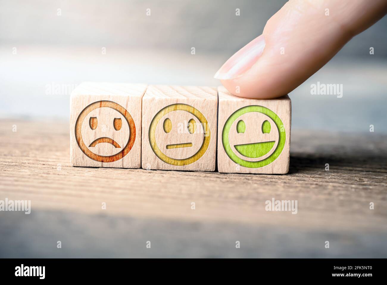 Gutes Feedback-Konzept mit roten, gelben und grünen Smileys auf Holzblöcken auf EINEM Brett wird der grüne Smiley von EINEM Finger berührt Stockfoto