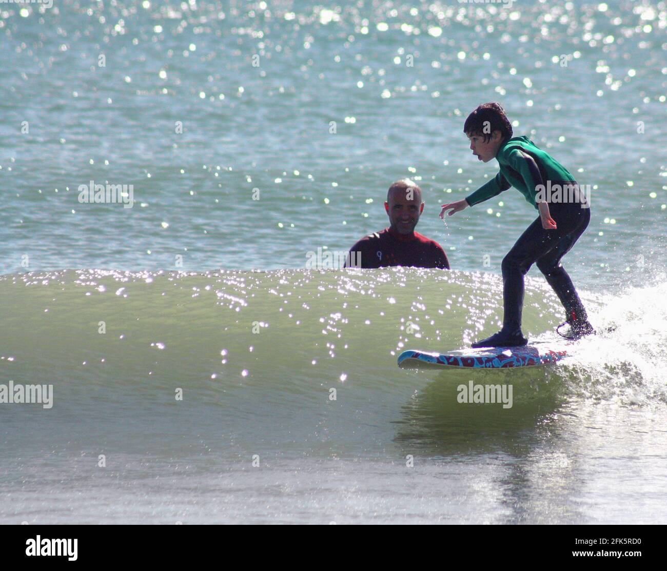 Kleiner spanischer Junge, der die Welle auf einem Surfbrett fängt Stockfoto