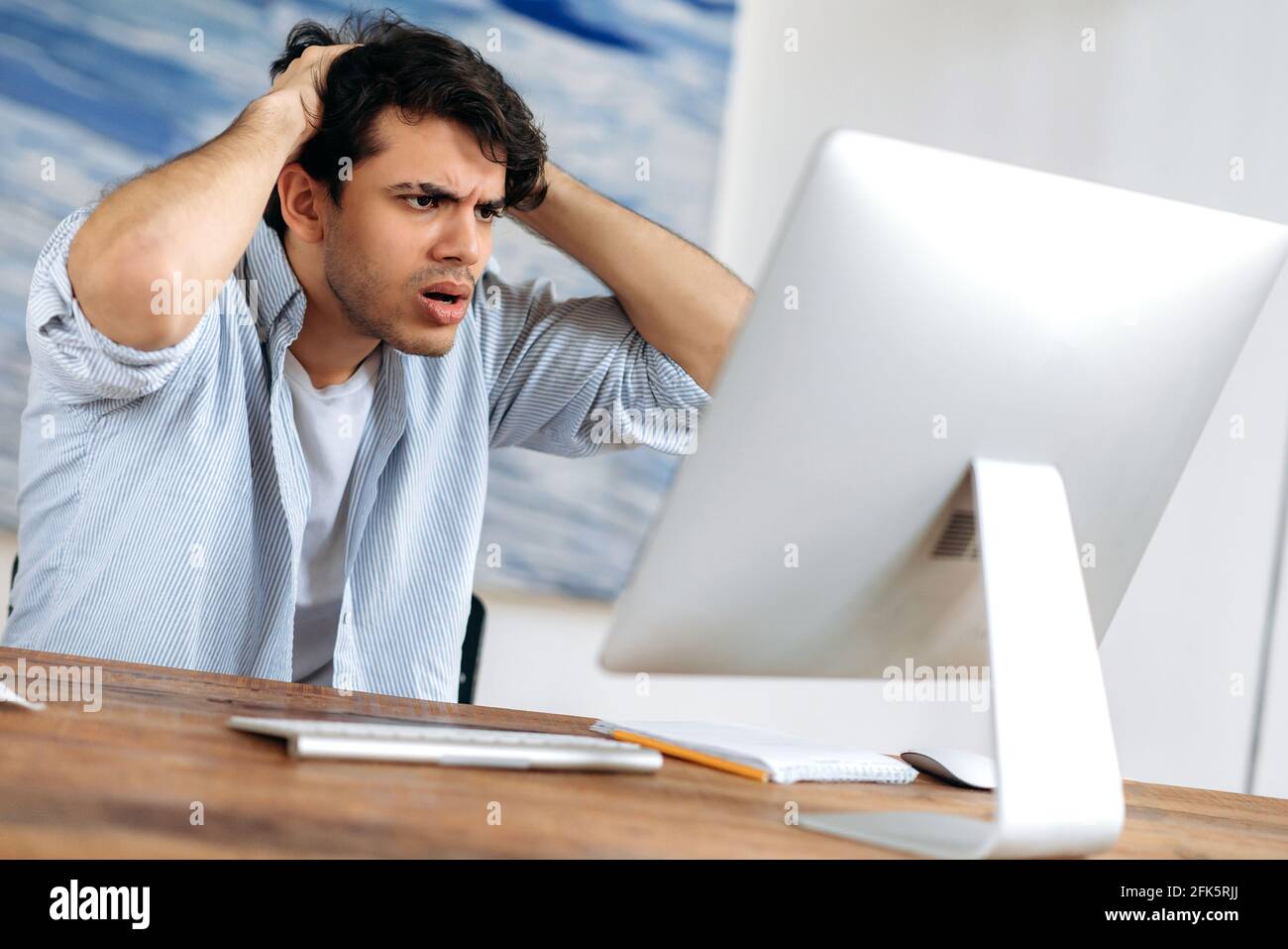 Schockiert ärgerte junge hispanische Broker, Freiberufler oder Geschäftsmann, der zu Hause am Computer arbeitete, hielt sich den Kopf fest, Geschäftsabschluss fiel durch, Niederlage, finanzieller Verlust, schaut ängstlich auf den Bildschirm Stockfoto