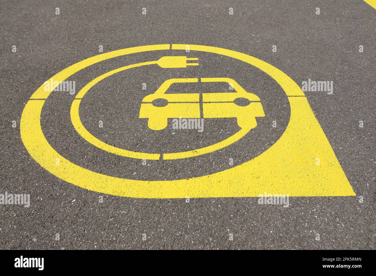 Niedrige Ansicht auf gelbem Symbol der Ladestation für Elektrofahrzeuge auf schwarzem Asphalt in der Stadt Zug, Schweiz Stockfoto