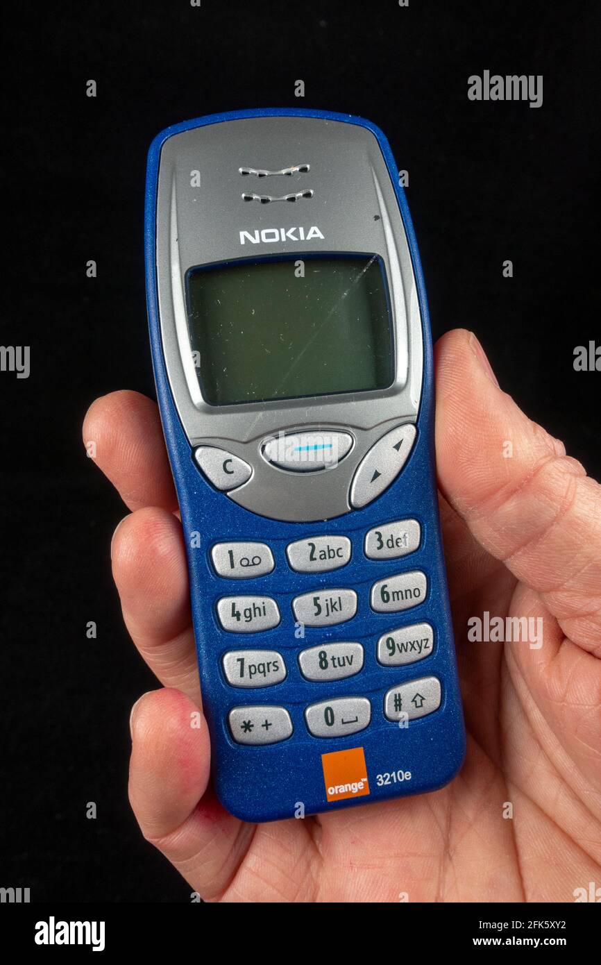 Ein Mann mit einem Orange Nokia 3210e-Telefon (das Nokia 3210e wurde ursprünglich 1999 veröffentlicht), Stockfoto