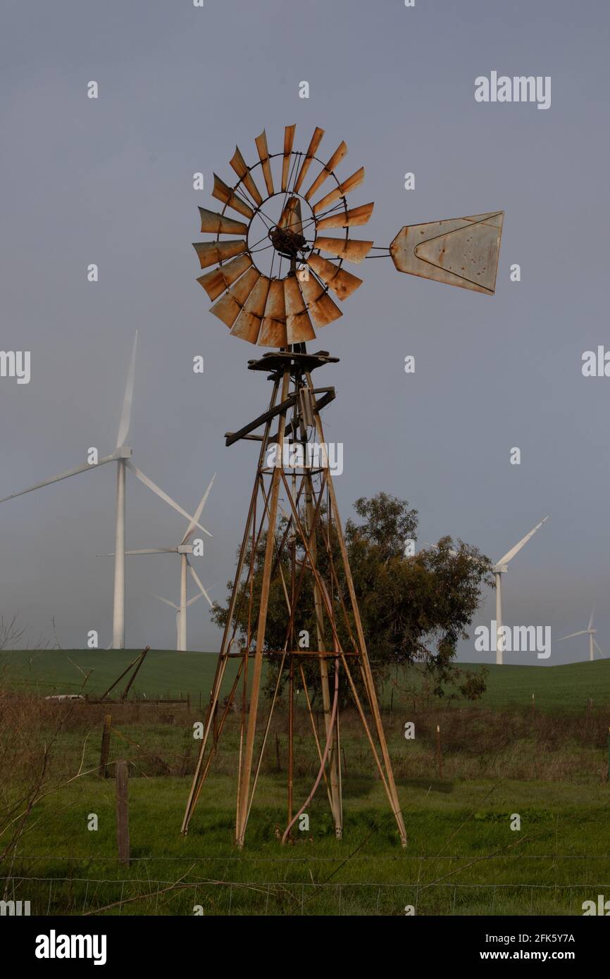 Eine legendäre, traditionelle Windmühle steht vor einer Reihe von Hightech-Windmaschinen, die auf privaten Weiden im kalifornischen Solano County aufgestellt sind. Stockfoto