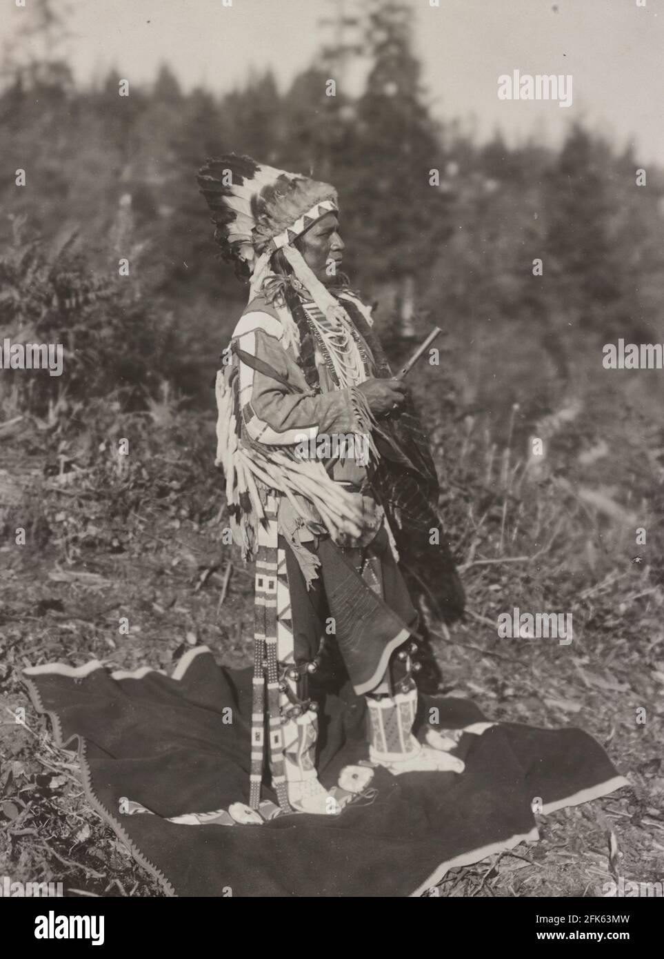 White Bird - Foto zeigt White Bird, einen Indianer aus der Region Plateau, Ganzkörperportrait, stehend, nach links gewandt, mit Federkopfschmuck - Frank Woodfield, 1911 Stockfoto