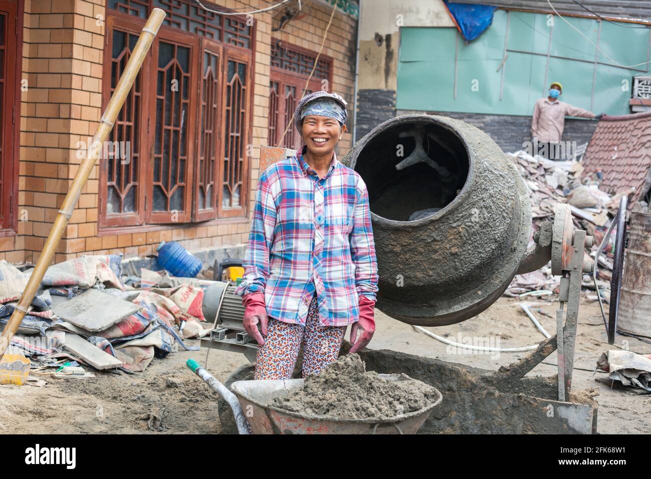 Fröhliche vietnamesische Handarbeiterin, die Beton im Zementmischer auf der Baustelle, Hoi an, Vietnam, mischt Stockfoto