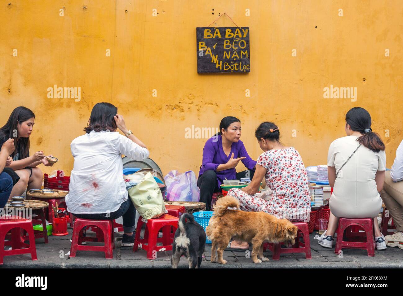 Vietnamesische Frauen saßen auf winzigen Hockern und aßen Straßenessen aus einem Straßencafé in Hoi an, Vietnam Stockfoto