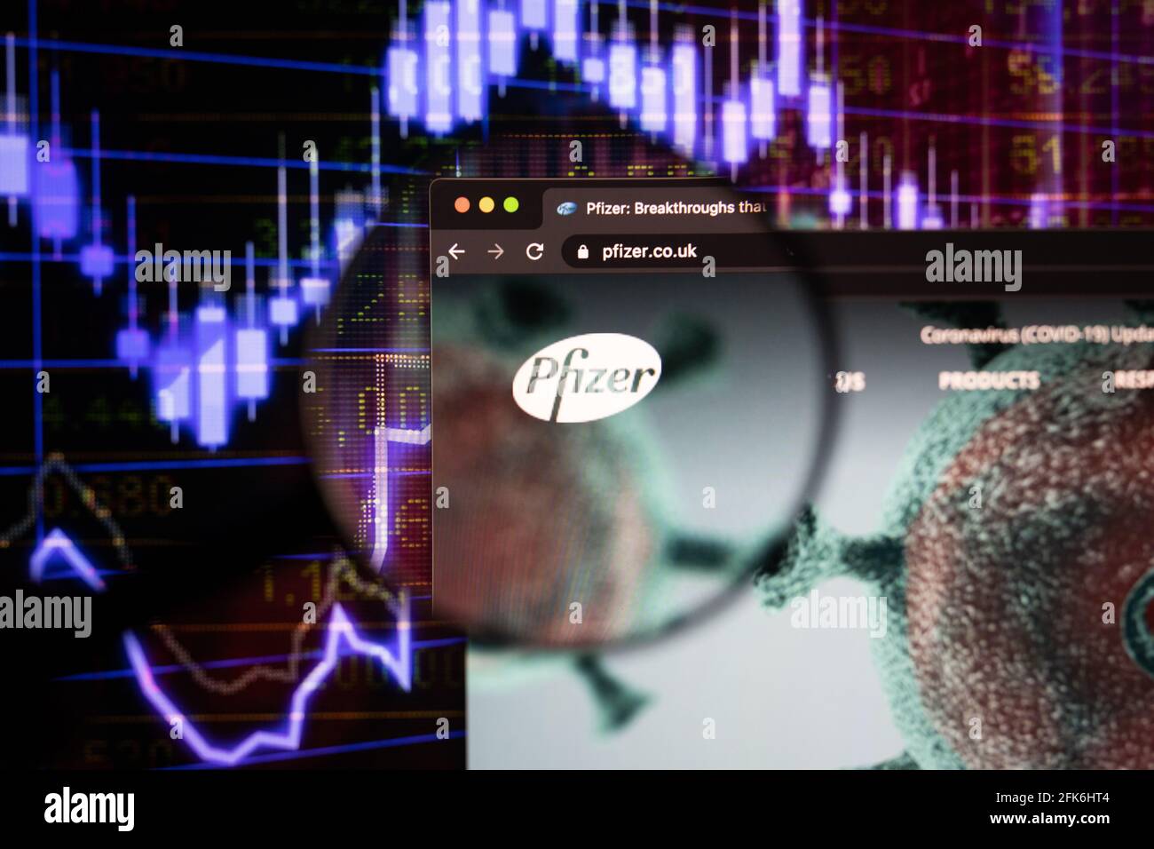 Das Firmenlogo von Pfizer auf einer Website mit verschwommenen Börsenentwicklungen im Hintergrund, die auf einem Computerbildschirm durch eine Lupe gesehen werden Stockfoto
