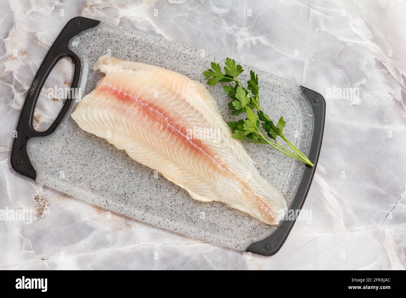 Filet aus rohem Pangasius-Fisch mit Petersilienblättern auf Schneidebrett. Draufsicht. Stockfoto