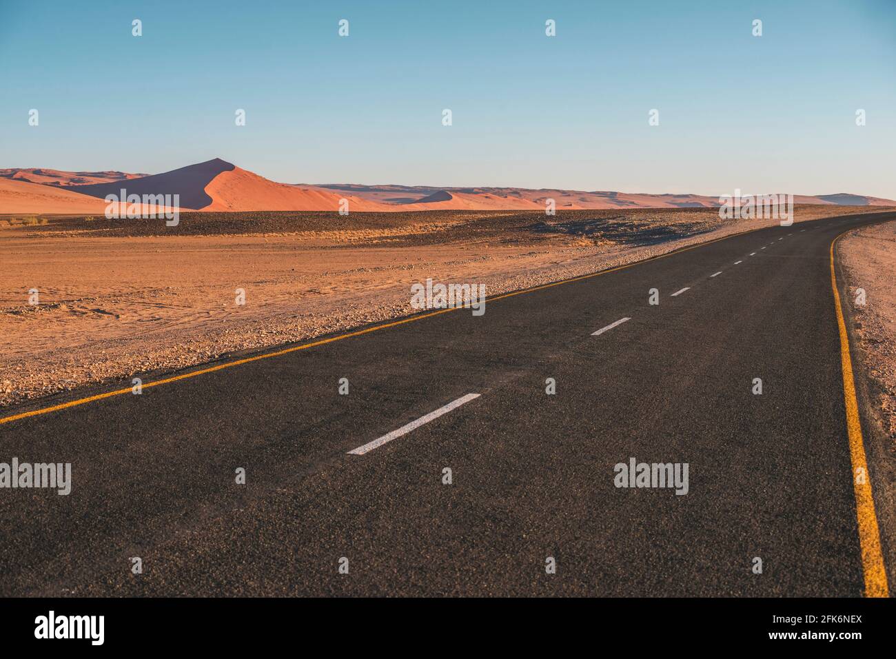 Leere Autobahn in Namibia mit roten Dünen Stockfoto
