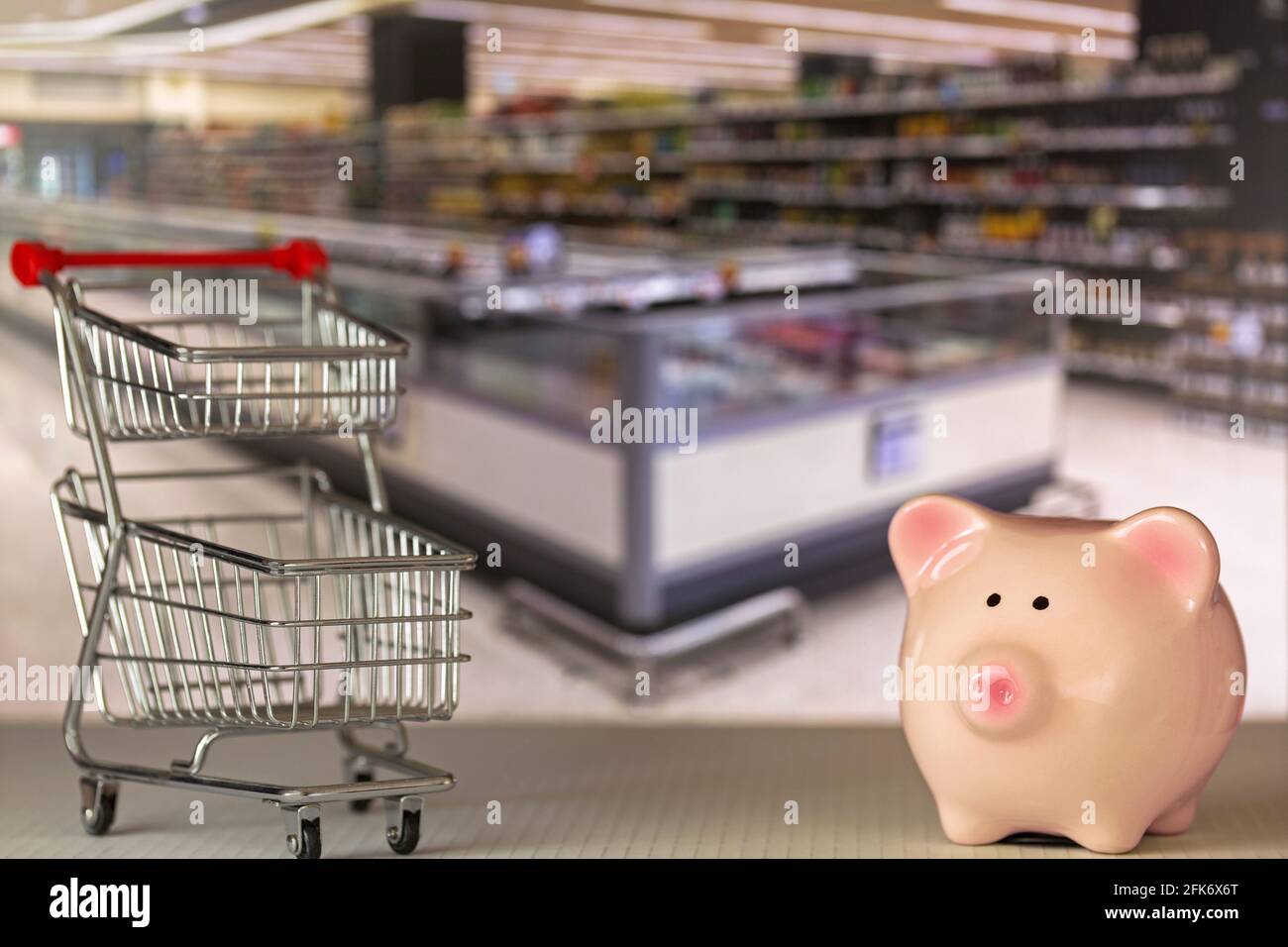 Pink Piggy Bank Schwein steht in der Nähe Mini-Shopping Push-Cart Mit verschwommenem Supermarkthintergrund Stockfoto