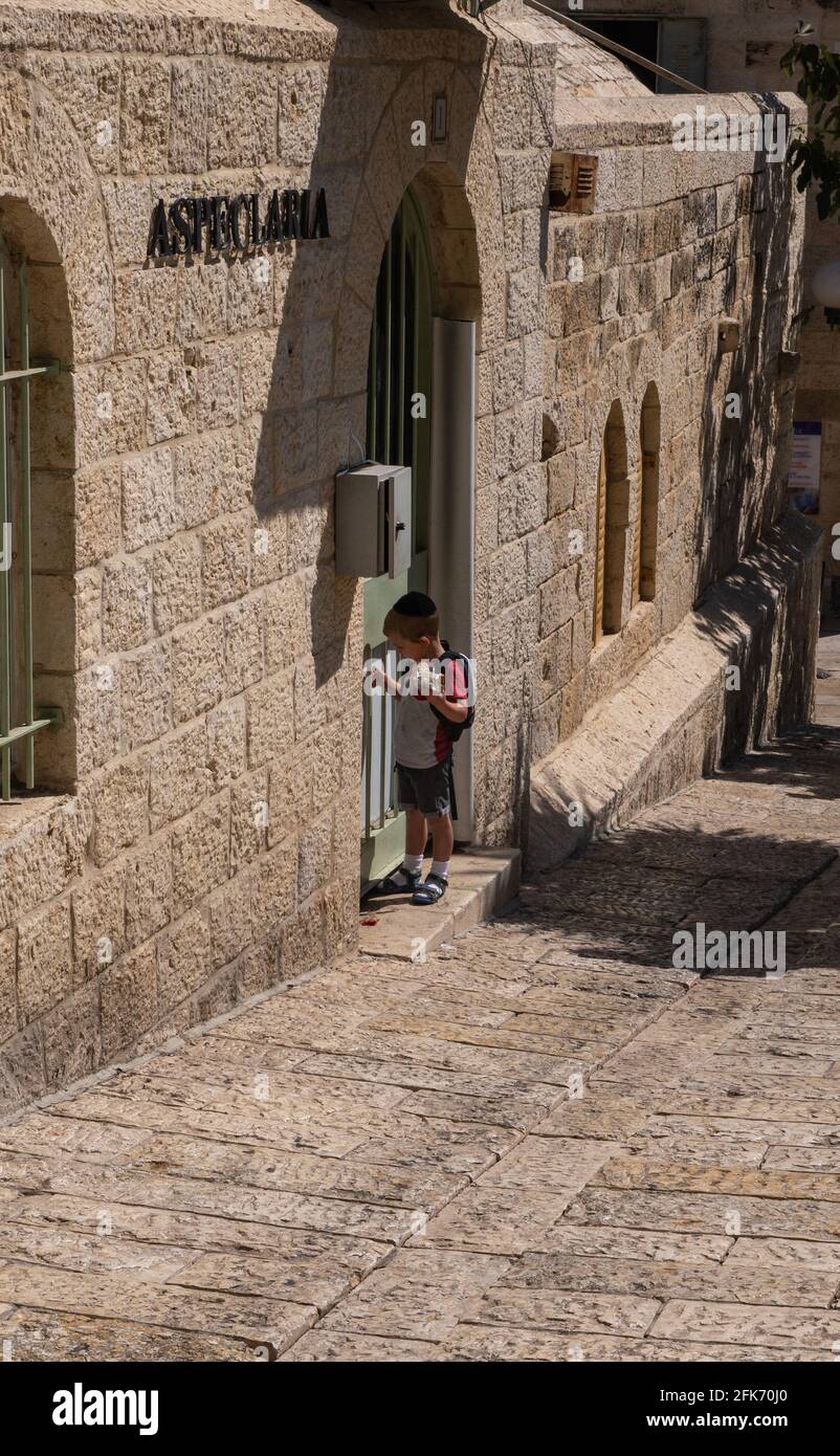 Alte Straße in Jerusalem. Kleiner jüdischer Junge klopft an die Tür. Heller, sonniger Tag Stockfoto