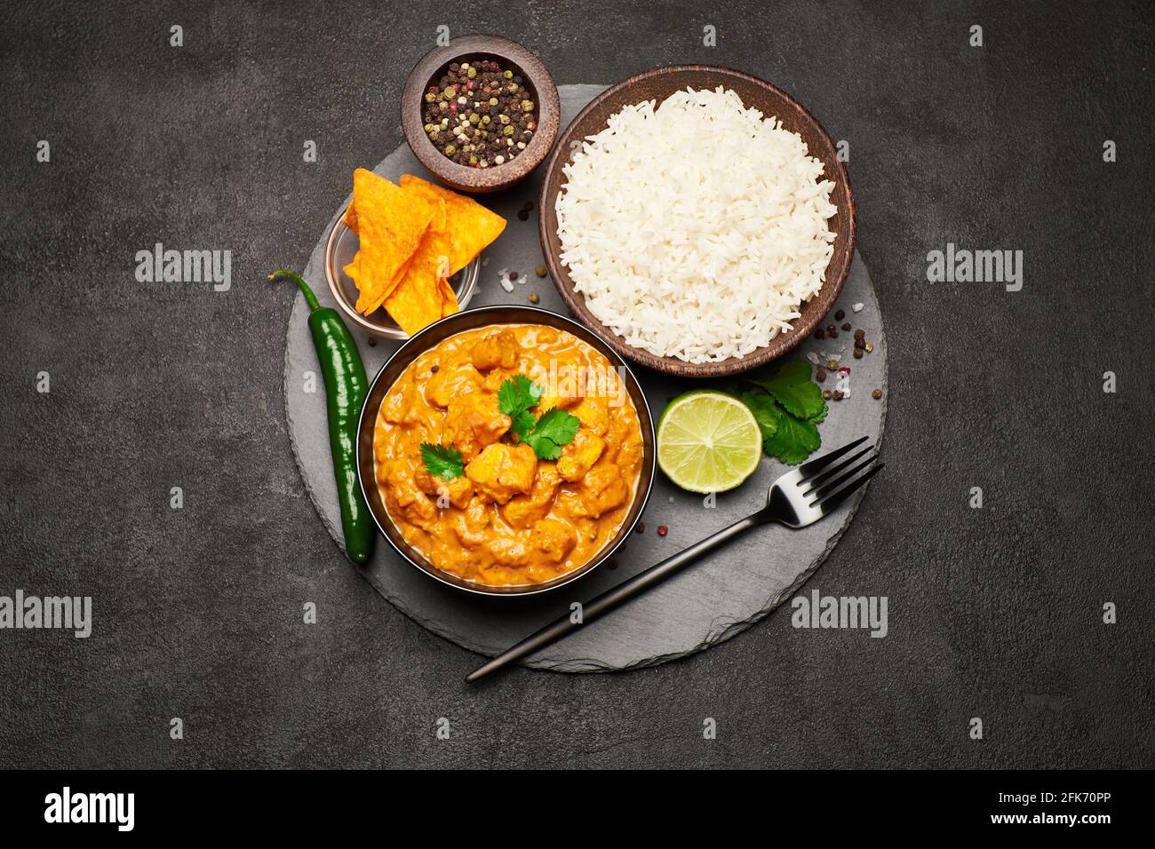 Teller mit traditionellem Chicken Curry, Nachos und Reis auf einem Servierbrett aus Stein Stockfoto