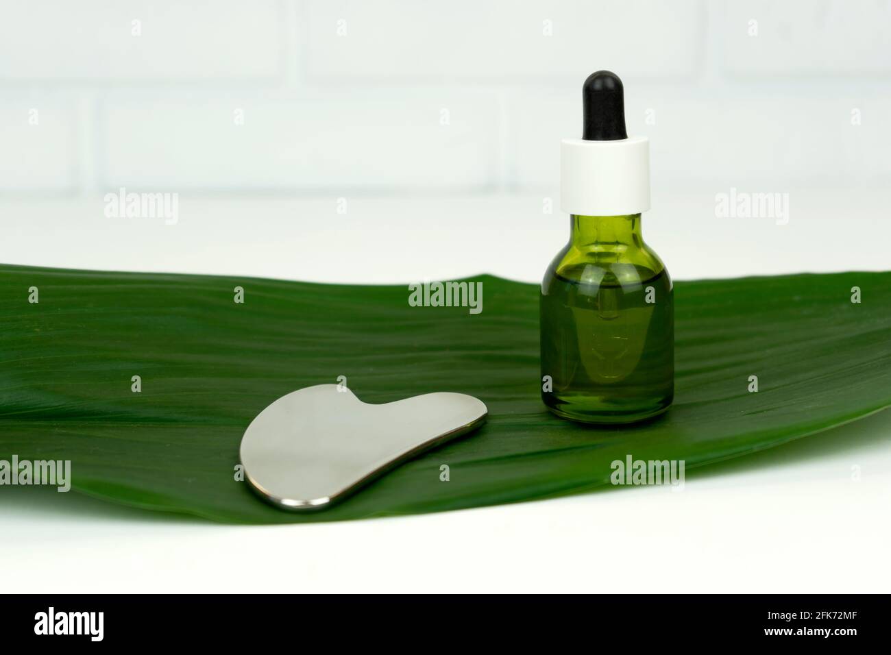 Ein nicht gebrandmarkt grünes CBD-Cannabisöl mit einem Gua Sha Massierende Kratzhilfe auf einem grünen Blatt liegen Stockfoto