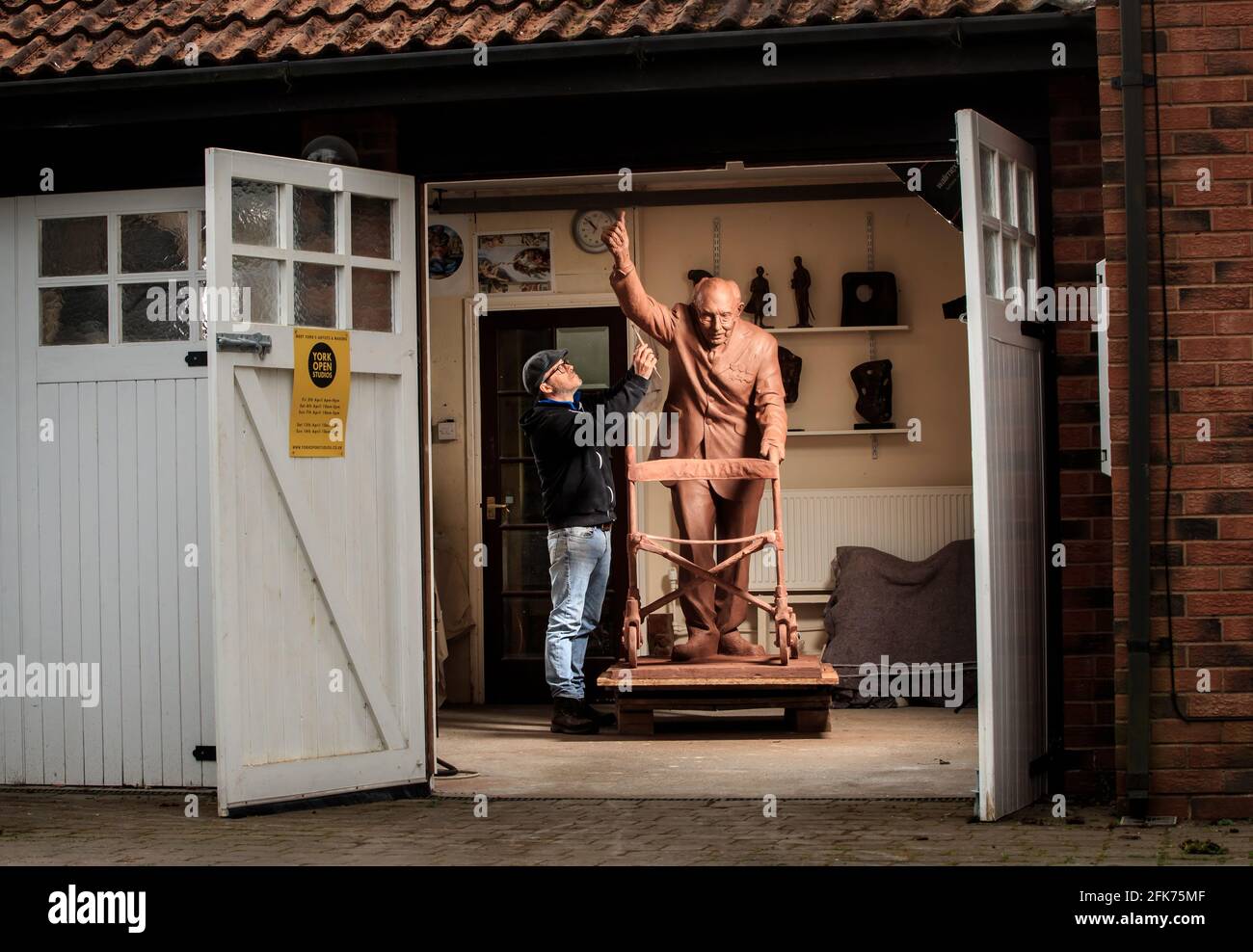 Andrian Melka verleiht seiner zwei Meter hohen Tonstatue von Captain Sir Tom Moore in seinem Atelier in der Nähe von York den letzten Schliff. Der Bildhauer ist Crowdfunding, um die Arbeit in Bronze gießen zu lassen, damit er sie dem Leeds Teaching Hospitals NHS Trust spenden kann. Bilddatum: Mittwoch, 28. April 2021. Stockfoto