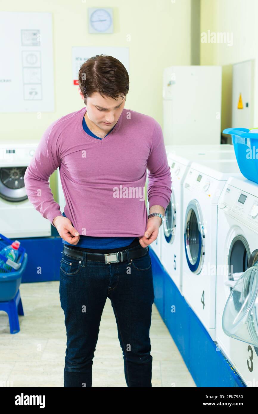 Junger Mann in einem Waschsalon, wäscht seine schmutzige Wäsche, im  Hintergrund sind Waschmaschinen, er ist wütend über sein unterdimensiones  Oberteil Stockfotografie - Alamy